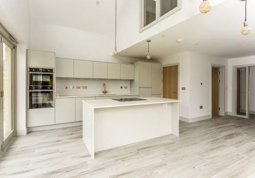 A modern white kitchen with built in oven and central island.