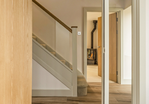 A view of the standard staircase leading up to the first floor at Milburn House with a view through the door next to the staircase of the fireplace in Lounge.